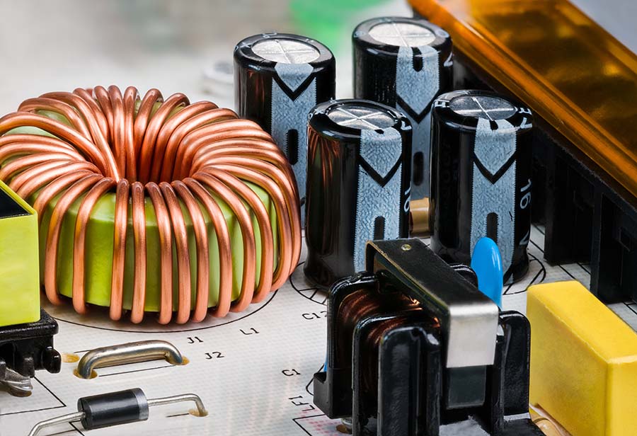 Toroidal core inductor, transformer or electrolytic capacitors on PCB detail. Close-up of coil wrapped by copper wire. Electrical components on white printed circuit board of switch-mode power supply.